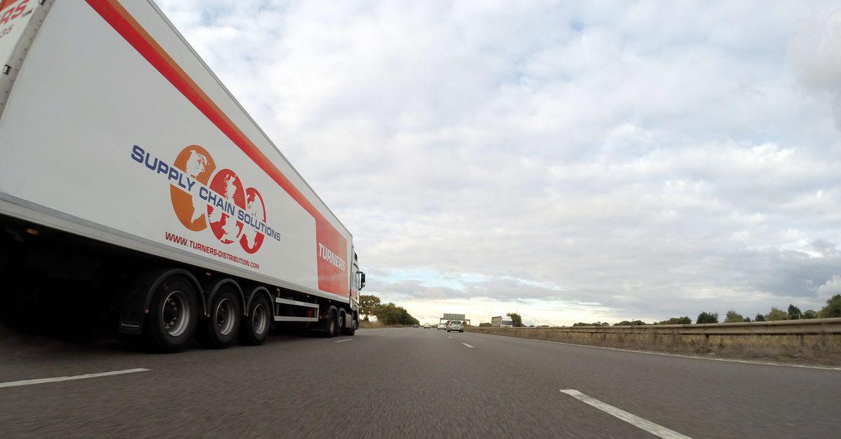A large semi truck labeled 'Supply Chain Solutions' travels down a highway under a cloudy sky.